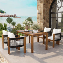 Outdoor dining set with wooden table and chairs on a patio by the sea.