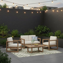 Outdoor furniture set with wooden chairs, table, and beige cushions against a brick wall.