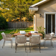 Outdoor patio set with wooden table and chairs on a concrete patio, surrounded by greenery.