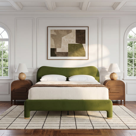 An olive green upholstered bed with a matching footboard and white bedding, styled in a bright, modern bedroom with white paneled walls, two wooden nightstands, table lamps, and a framed abstract painting above the headboard.